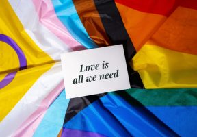 A note reading "Love is all we need" sits on top of a pride flag.
